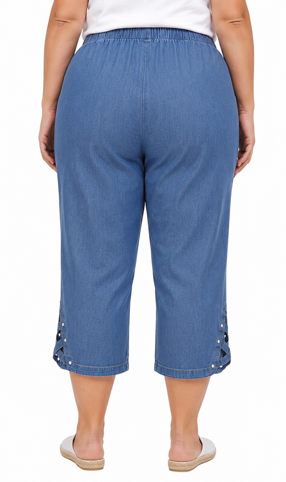 A person shown from the back wearing blue cropped pants with decorative side lacing and silver eyelet details near the hem, paired with a white top and flat espadrille-style sandals on a light gray studio background.